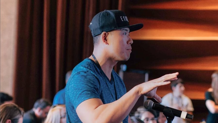 Mike speaking on stage at a coaching event, gesturing while addressing an audience